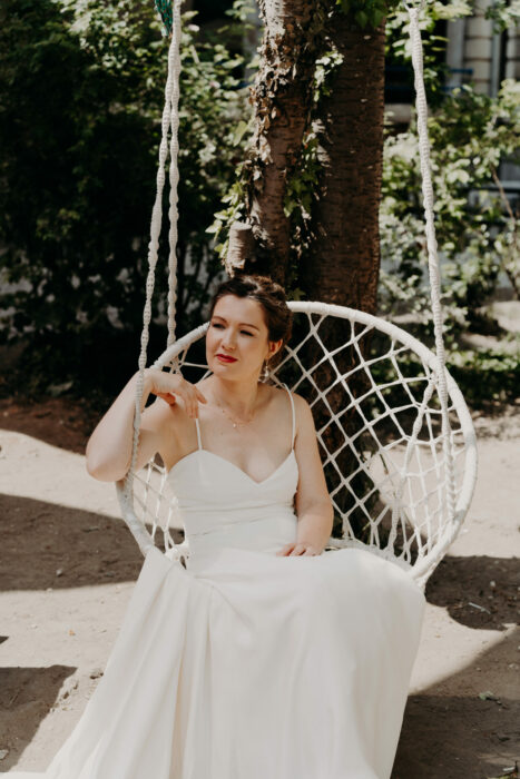 Mariée assise sur balançoire avec une robe de mariée en soie et portant un collier Atelier Armande