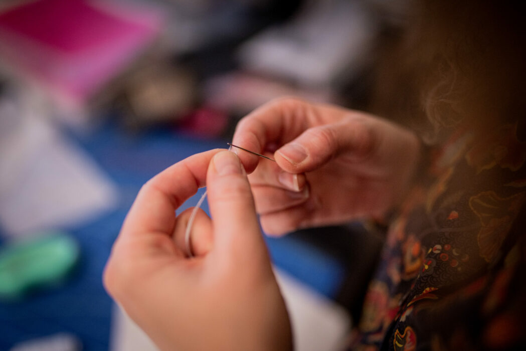 Créatrice de la maison AU FIL D'UN JOUR qui enfile du fil dans son aiguille pour couture fine à la main